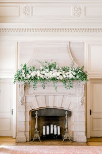 White carnations are lavishly heaped upon the mantle of a classical fireplace